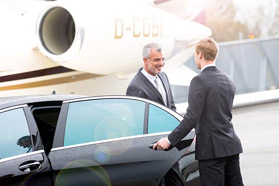 Ein Chauffeur gibt einem Fahrgast die Hand neben einer Limousine.